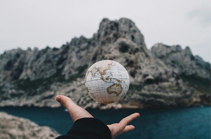 Mano sosteniendo un globo terráqueo con montañas y mar de fondo.